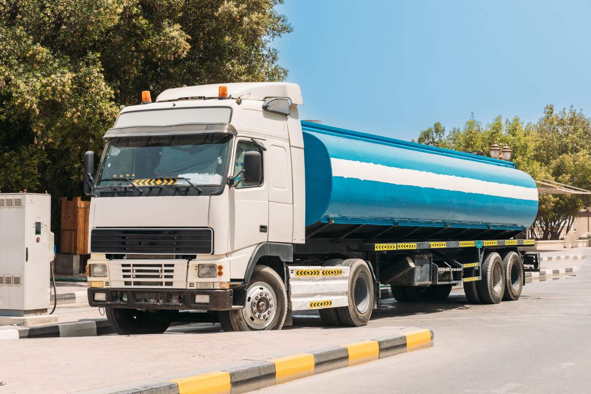 Water tank trailer unit, prime mover, refuel at gas and oil station in sunny summer day. Water tank trailer parked near oil station. Water tank trailer unit, prime mover, refuel at gas and oil station in sunny summer day.