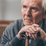 close up of retired man with grey hair holding walking cane