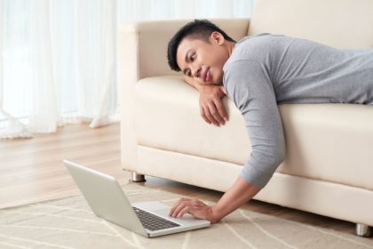 Lazy young Vietnamese man lying on sofa and watching something on laptop