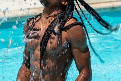 Black man with afro hair and dreadlock hairstyle comes out of the pool splashing water