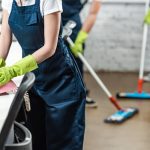 cropped view of a cleaning service agent wiping phone while colleagues washing floor with mops