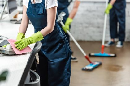 cropped view of a cleaning service agent wiping phone while colleagues washing floor with mops